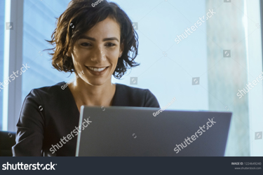 Stock Photo Confident Female Executive Works On A Laptop Sitting At Her Desk In Modern Office With Big City 1224649240